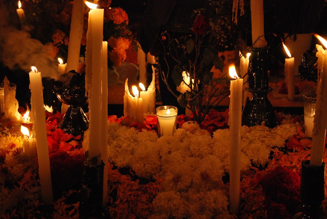 Tall candles and a glass votive glow among flowers in the darkness.
