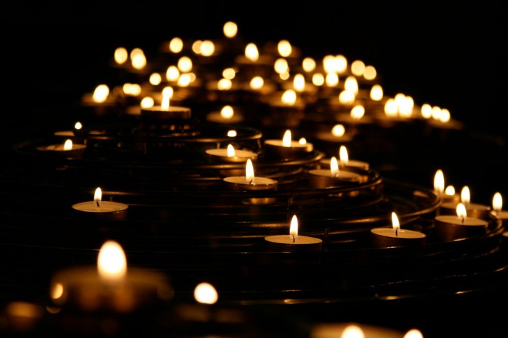Rows of small burning candles recede into the darkness.